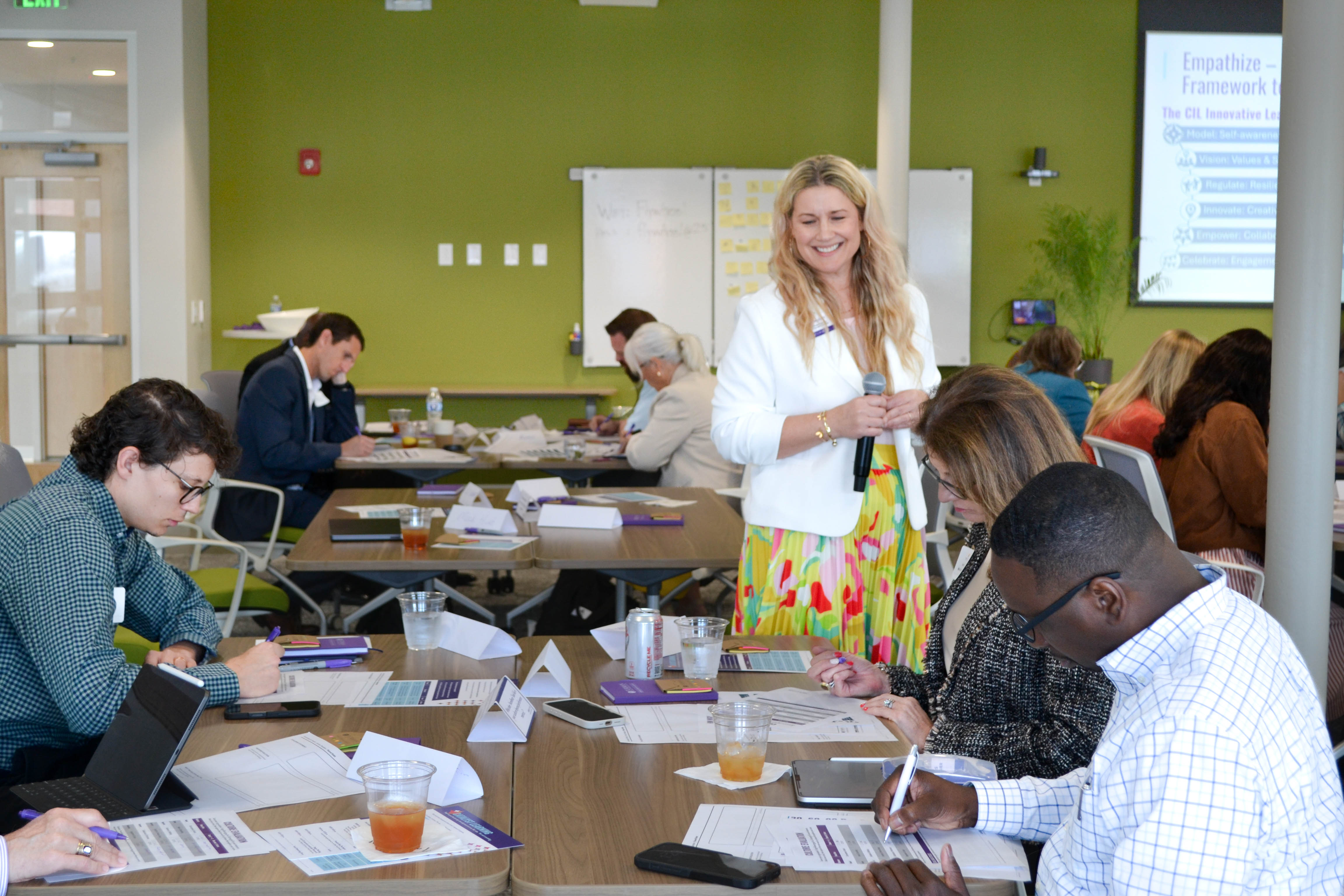 Sarah Waylett stands at a desk of 4 people, who are working on writing on paper.